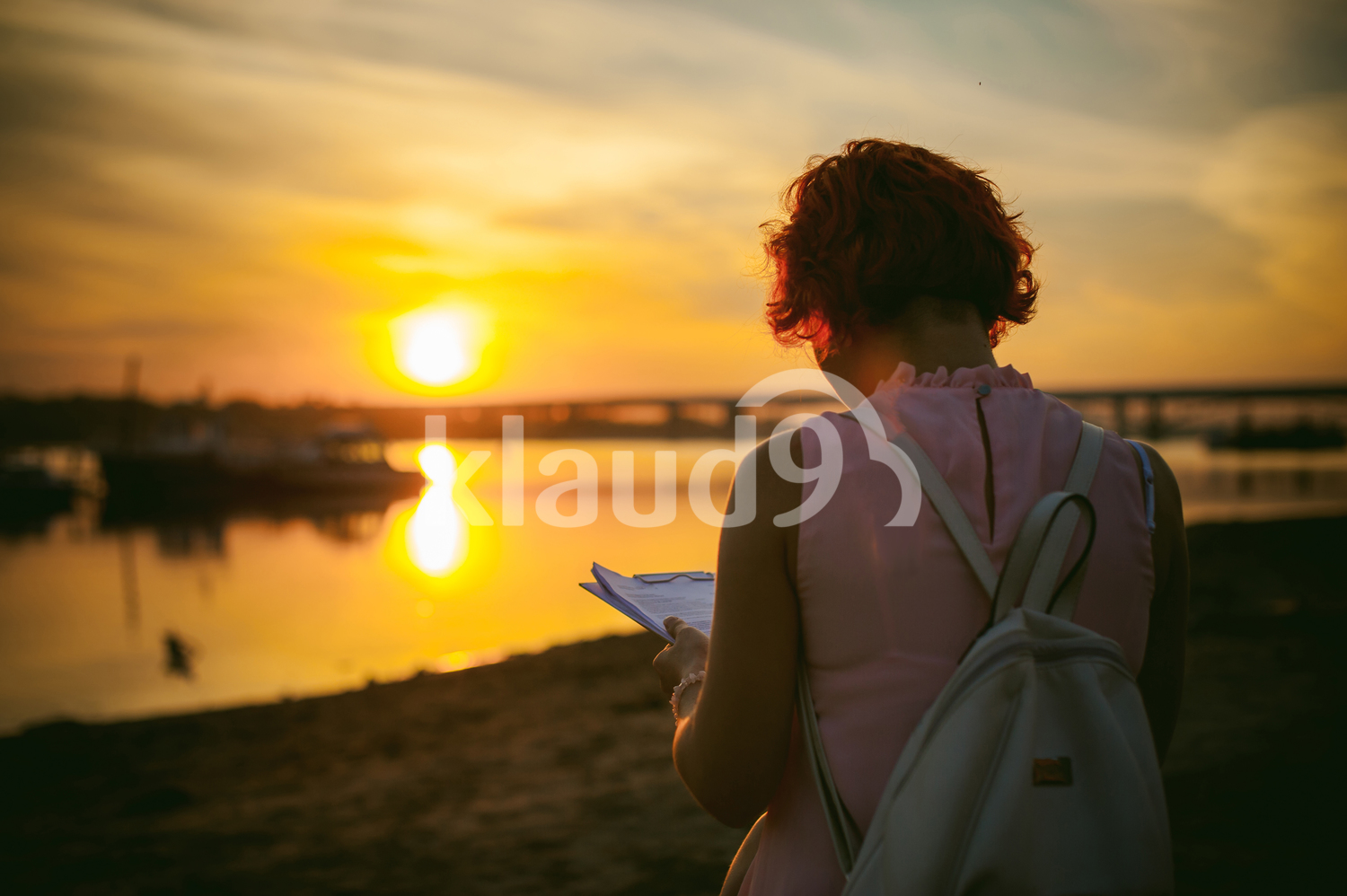 Woman with dyed red hair in a pale pink dress against a beautiful sunset