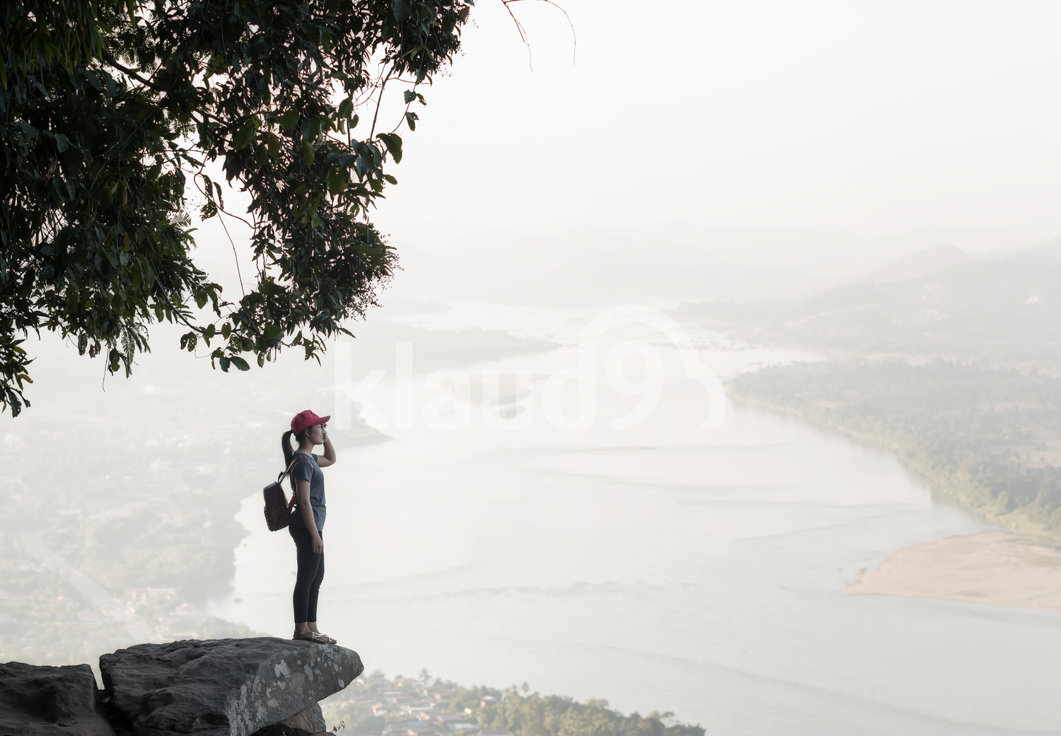 Young woman standing on cliff's edge and looking into a wide valley