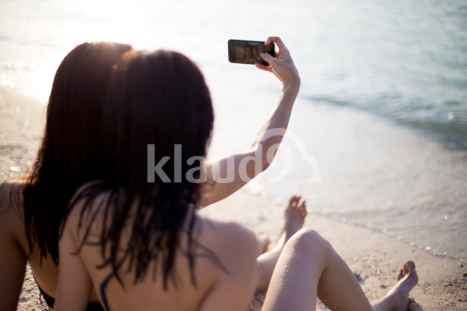 Back view of two friends taking a selfie on the beach