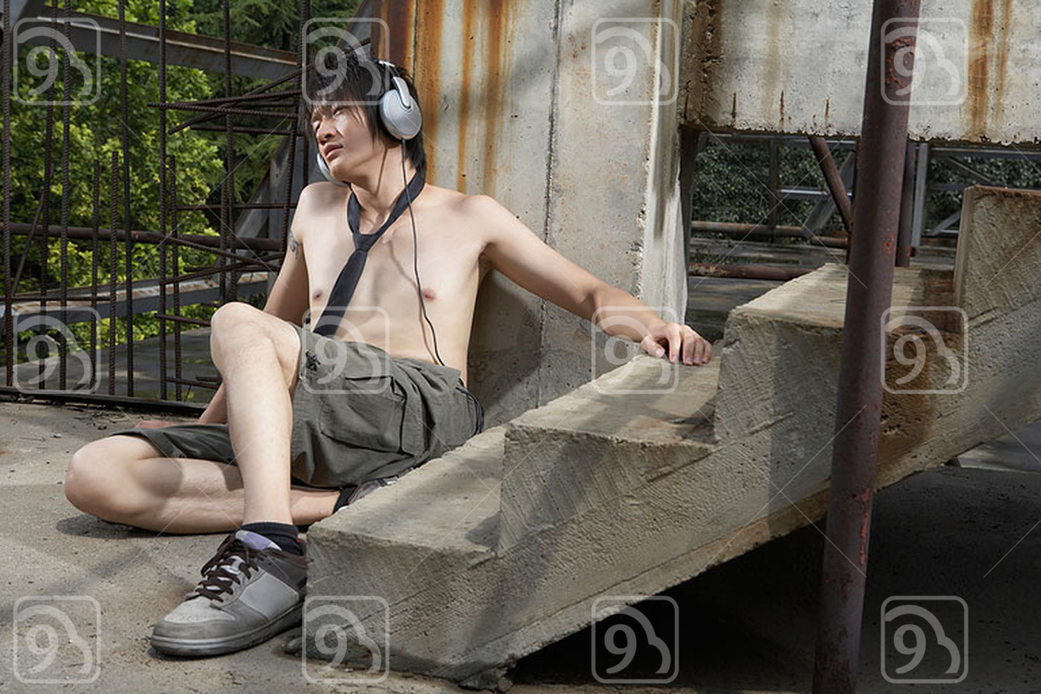 Shirtless young Chinese man wearing headphones in construction site 
