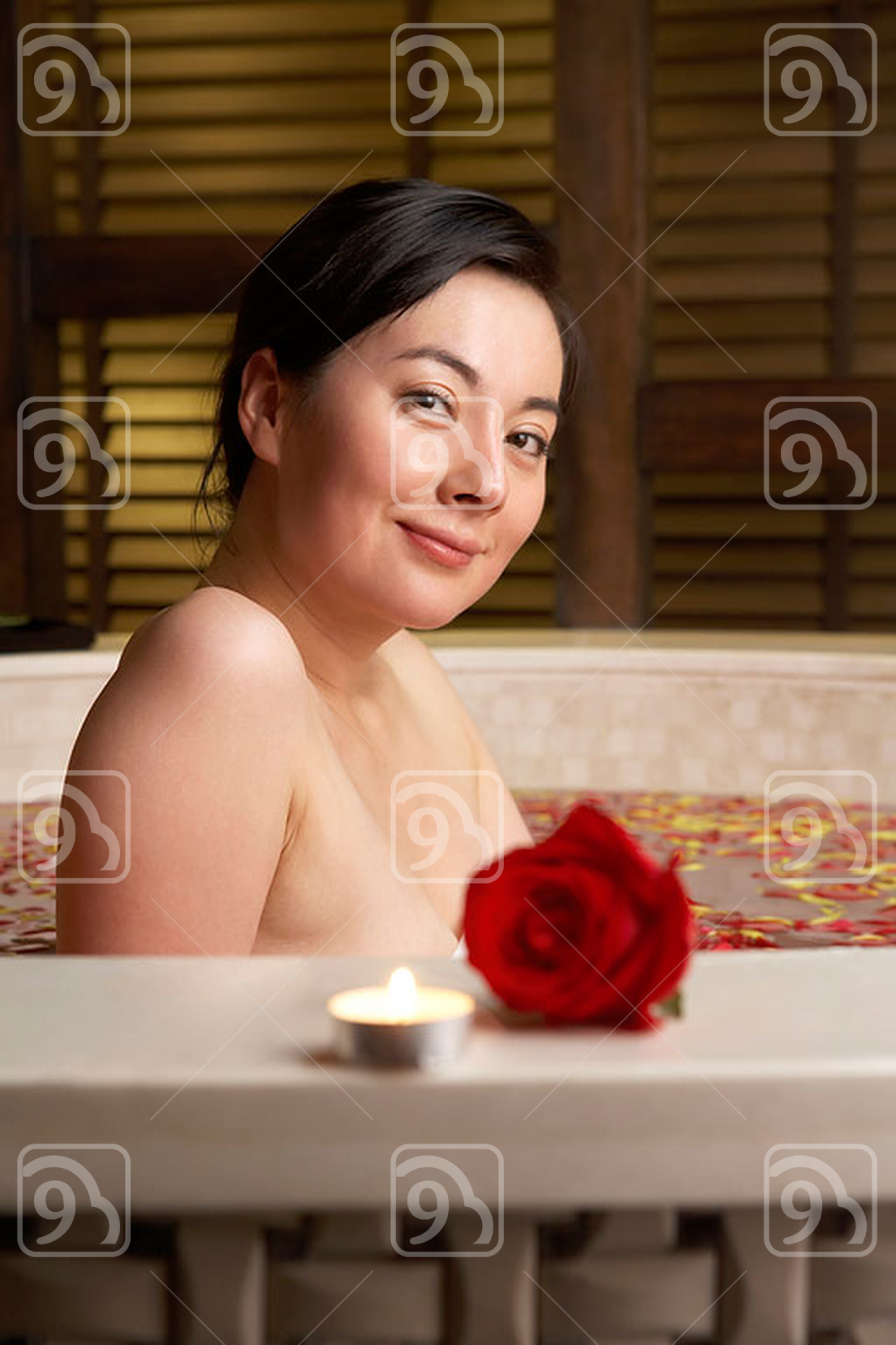 Chinese woman relaxing in a rose petal bath with a rose and candle 