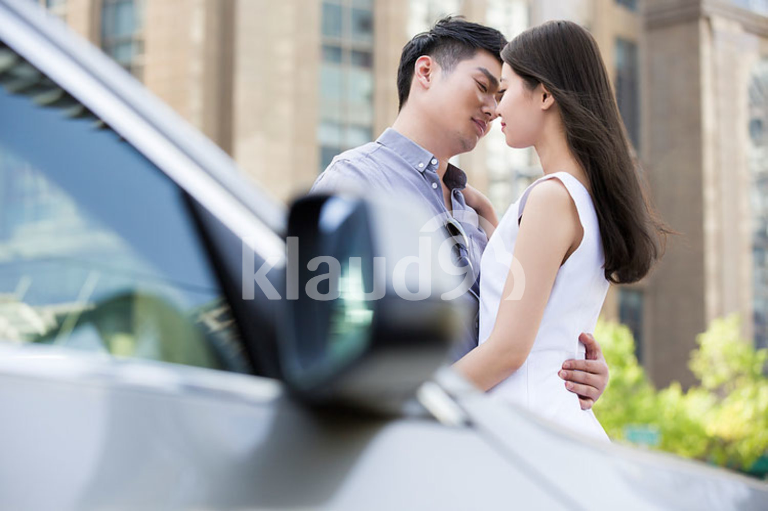 Young Chinese couple kissing next to their car