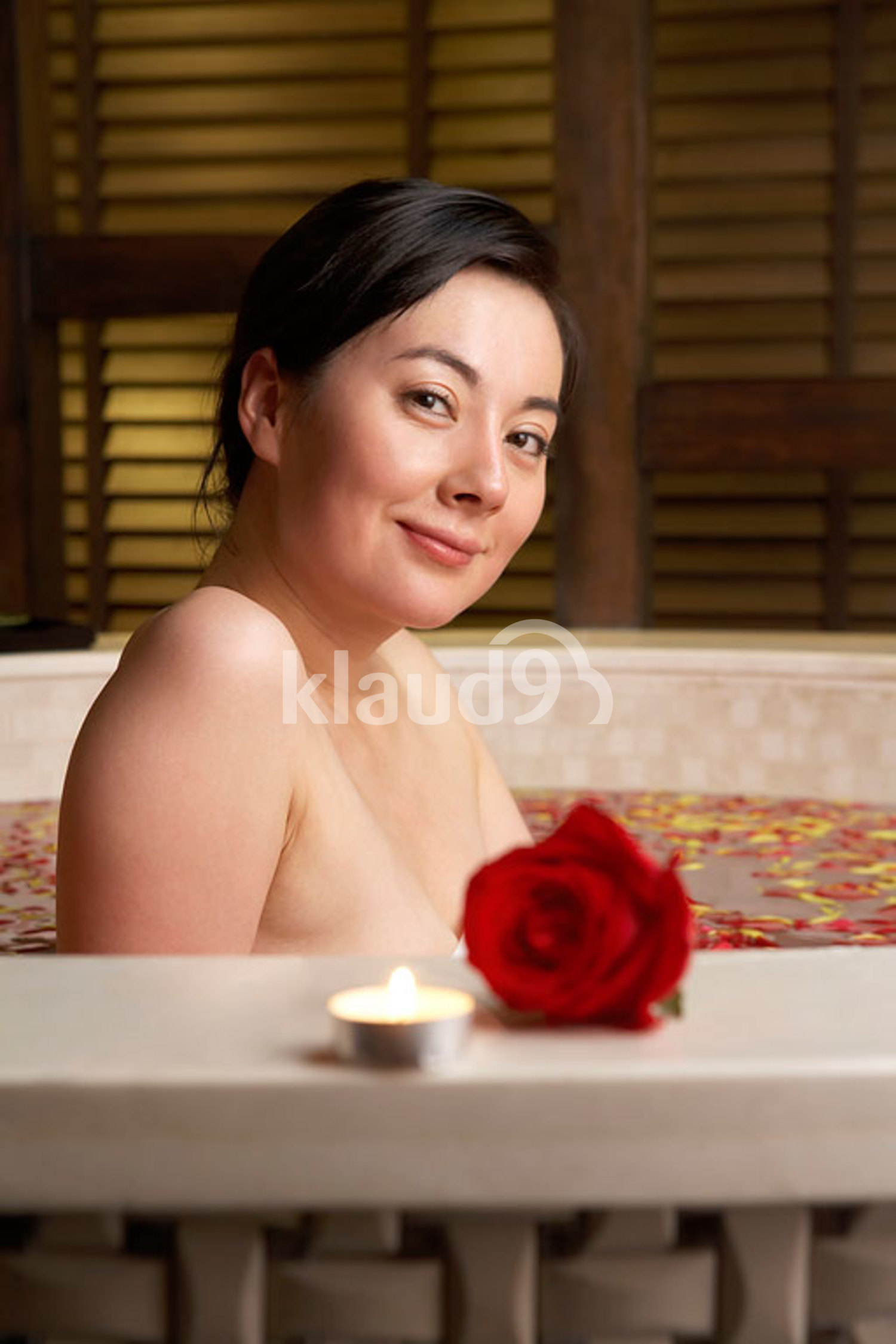 Chinese woman relaxing in a rose petal bath with a rose and candle