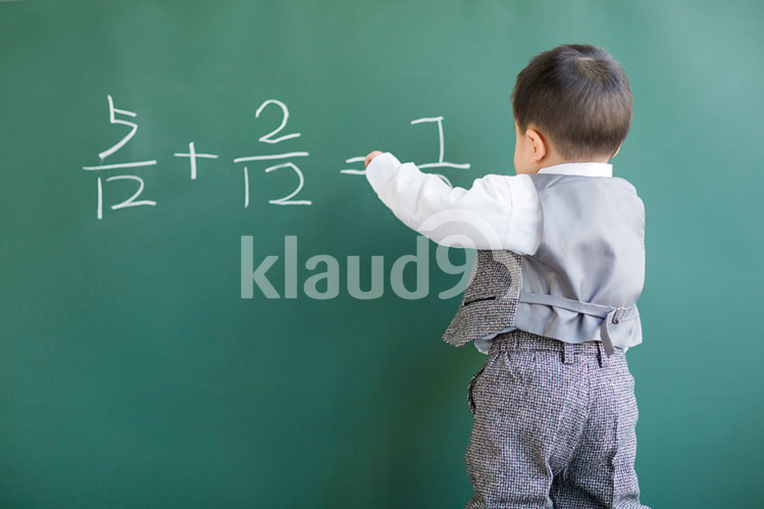 Cute Chinese baby doing mathematics on blackboard