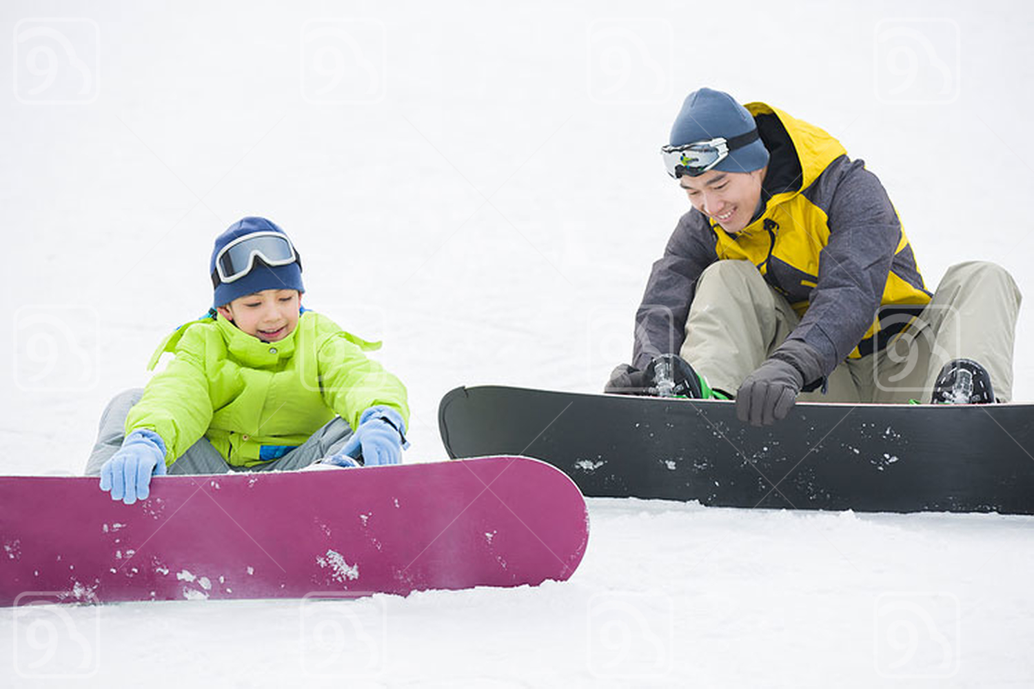 Young Chinese father and son with snowboards on the snow 