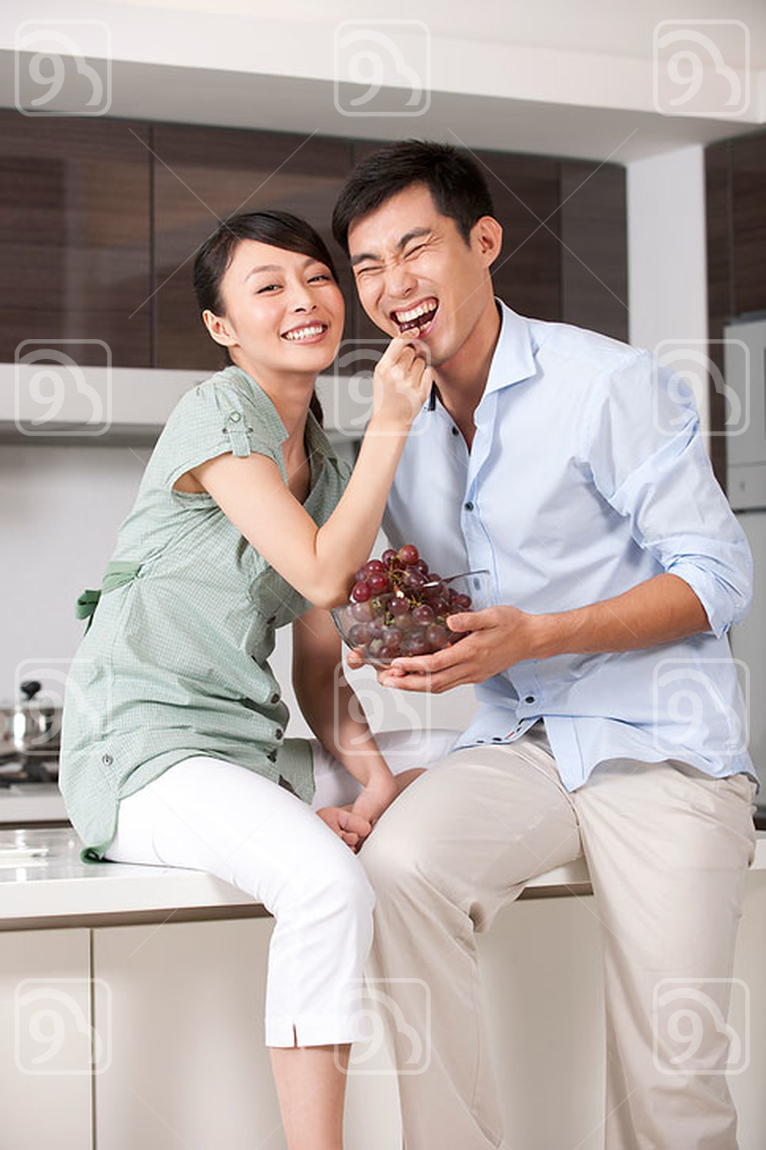 Chinese woman feeding man grapes in the kitchen 