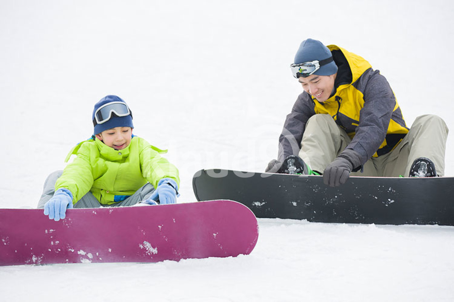 Young Chinese father and son with snowboards on the snow