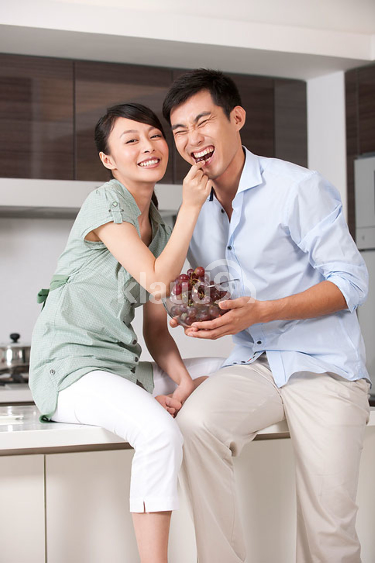 Chinese woman feeding man grapes in the kitchen