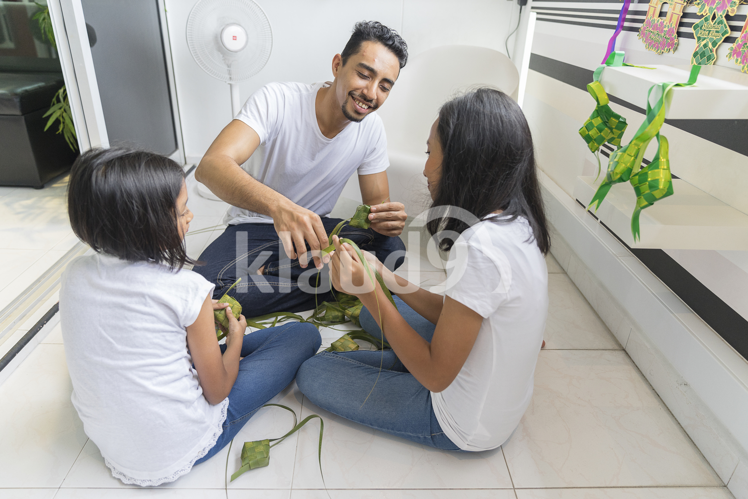 Young father teaching his kids how to make ketupat.