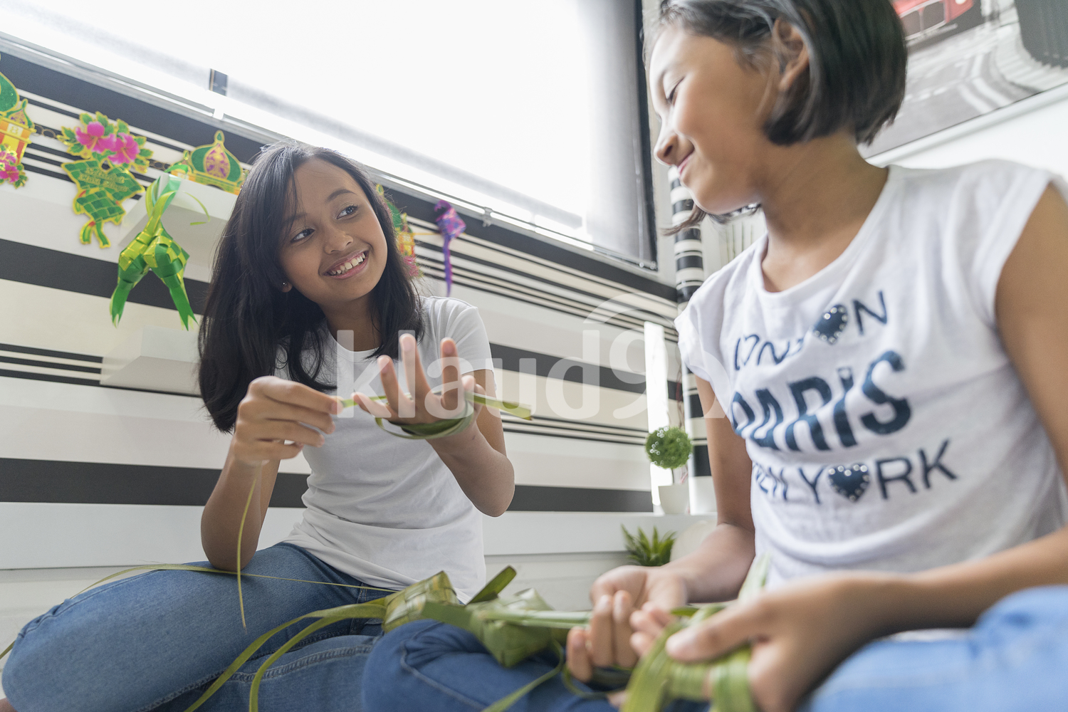 Young girl teaching her sister on how to make ketupat.