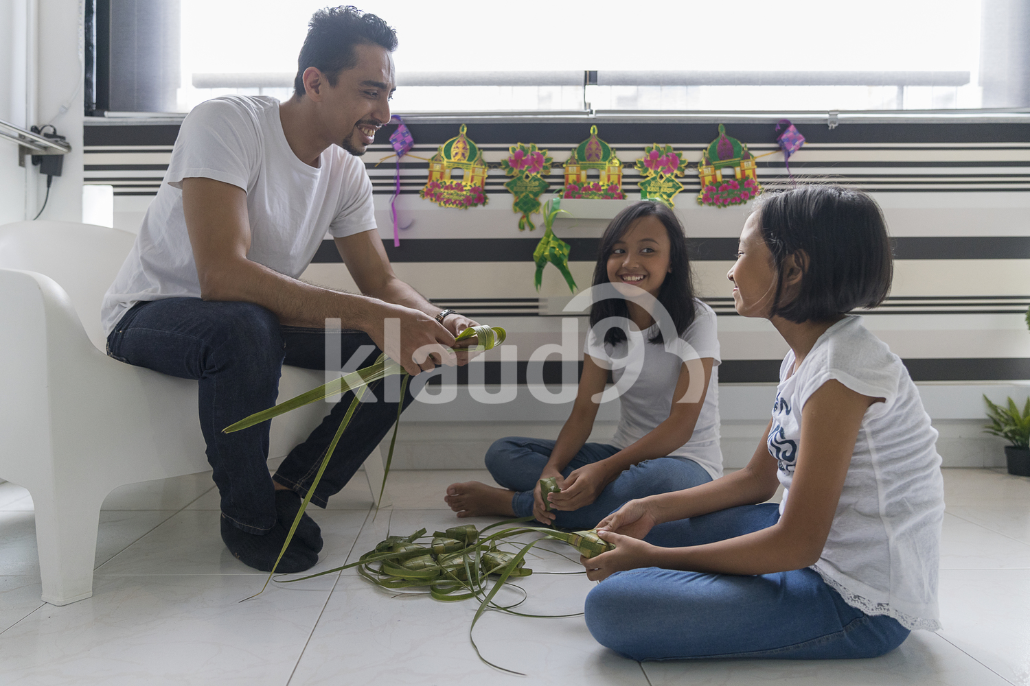 Father teaching his kids how to make ketupat at home for Hari Raya