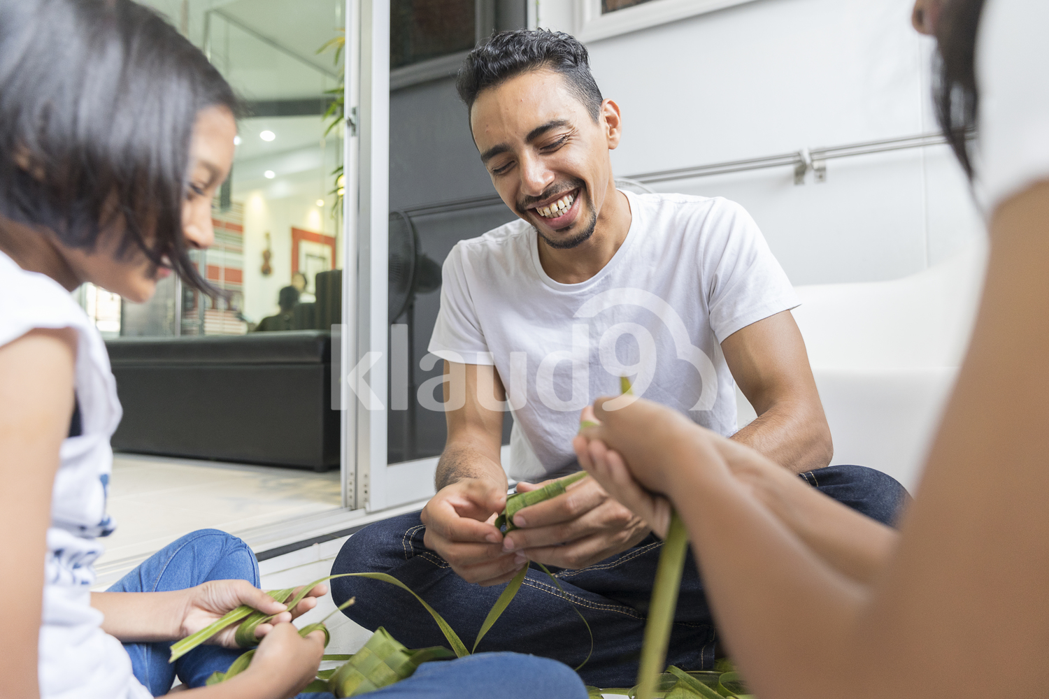 Cheerful Father teaching his kids how to make ketupat