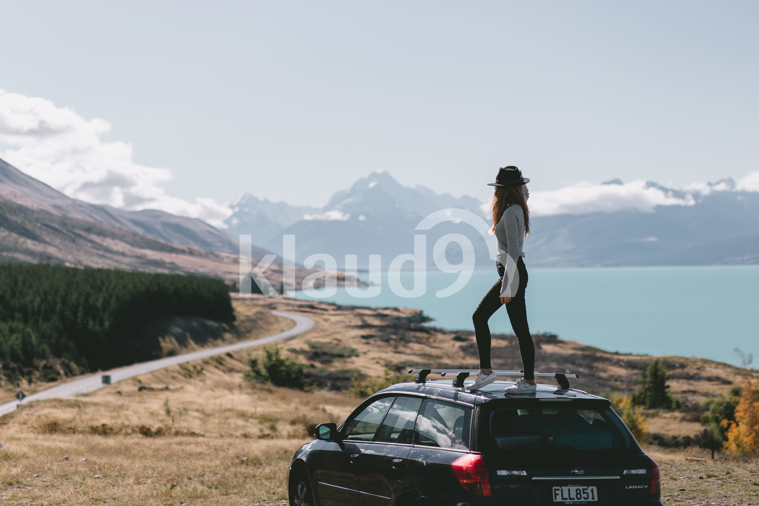 Young woman standing on top of car in Milford Sound, New Zealand