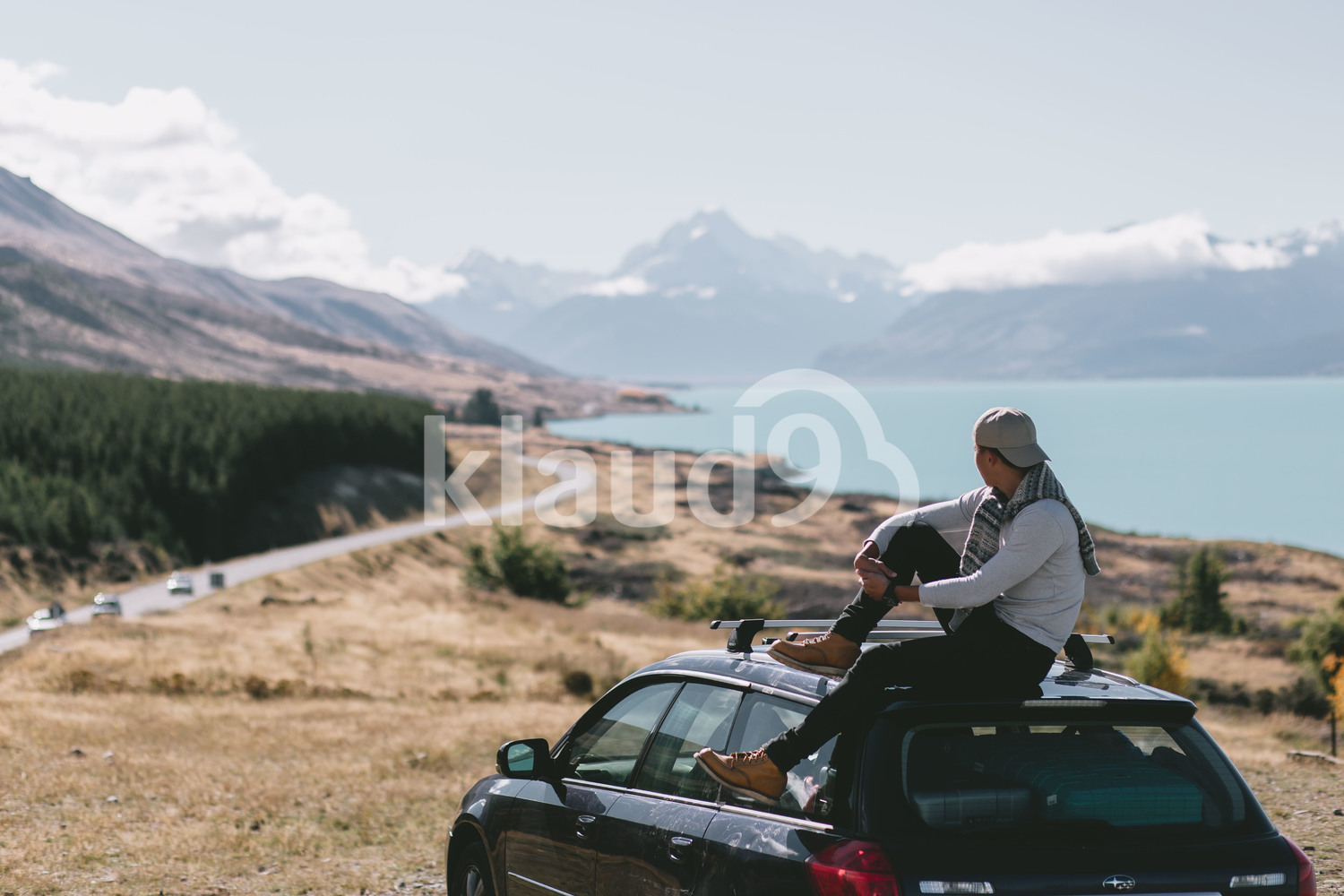 Back view of young man sitting on top of car in Milford Sound, New Zealand