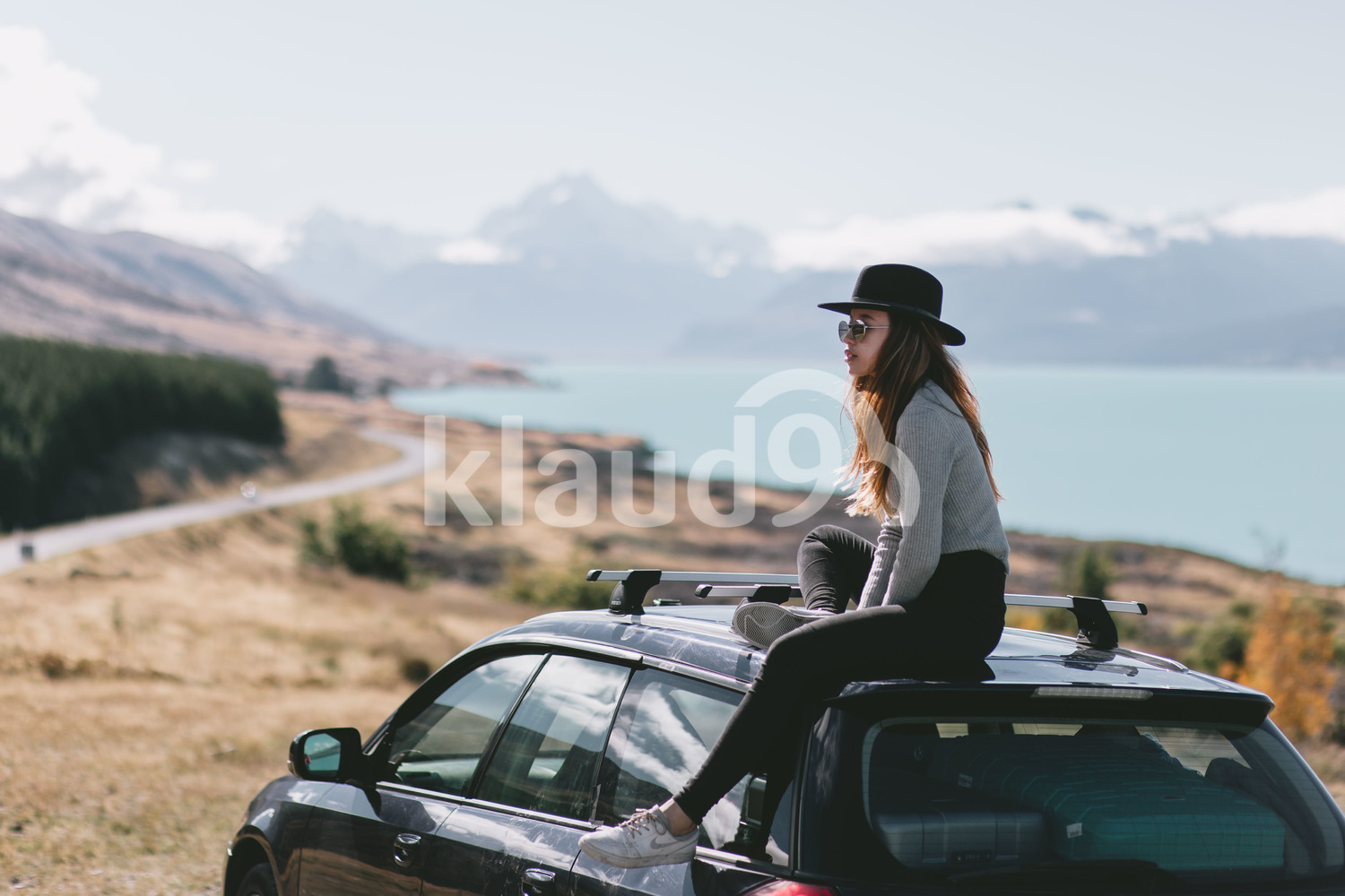 Young woman sitting on top of car in Milford Sound, New Zealand