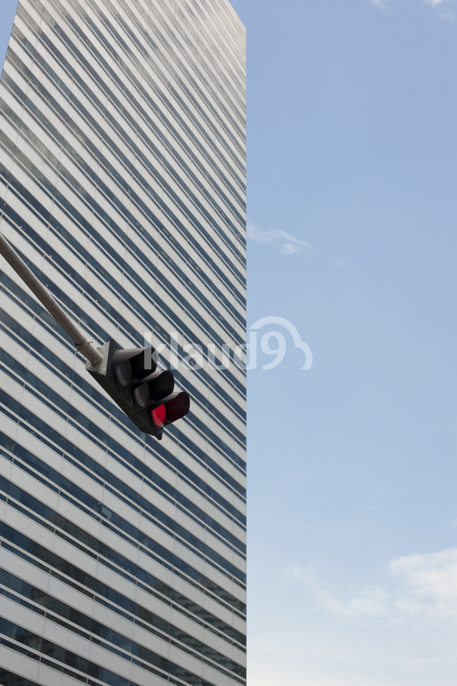 Skyscraper with red traffic light in the foreground against blue skies