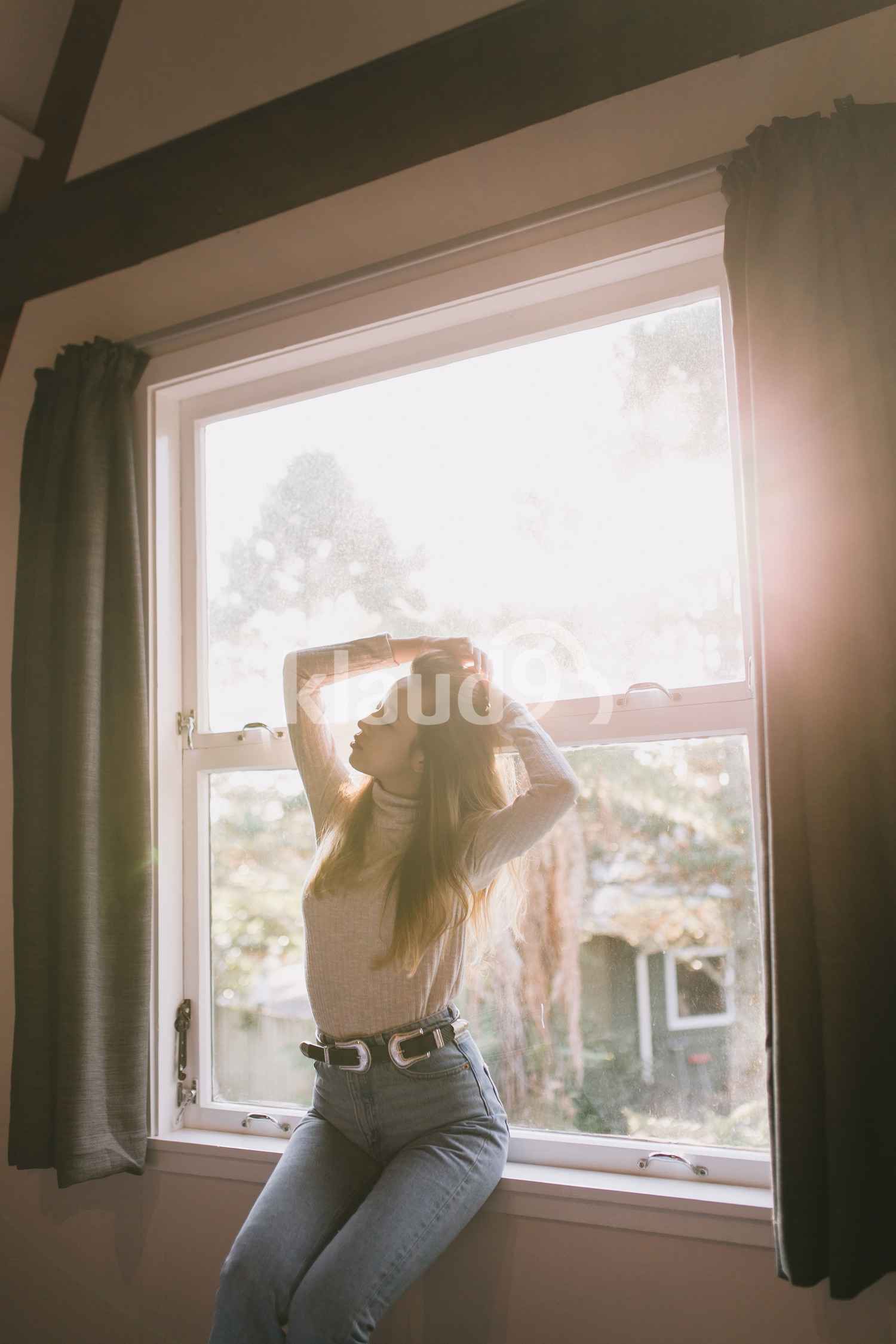 Young woman sunbathing by the window at her home in Queenstown, New Zealand
