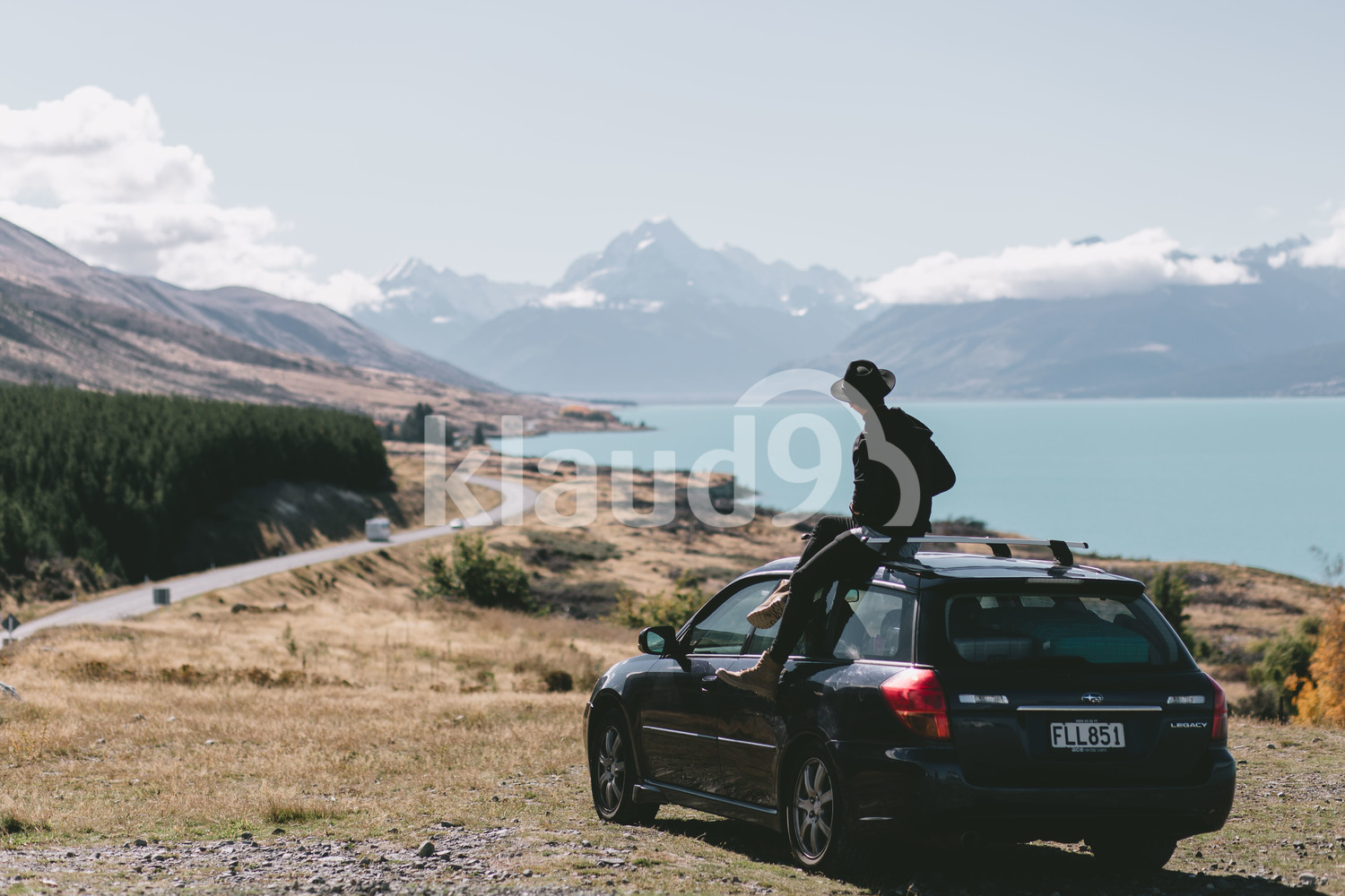 Back view of young man sitting on top of car in Milford Sound, New Zealand