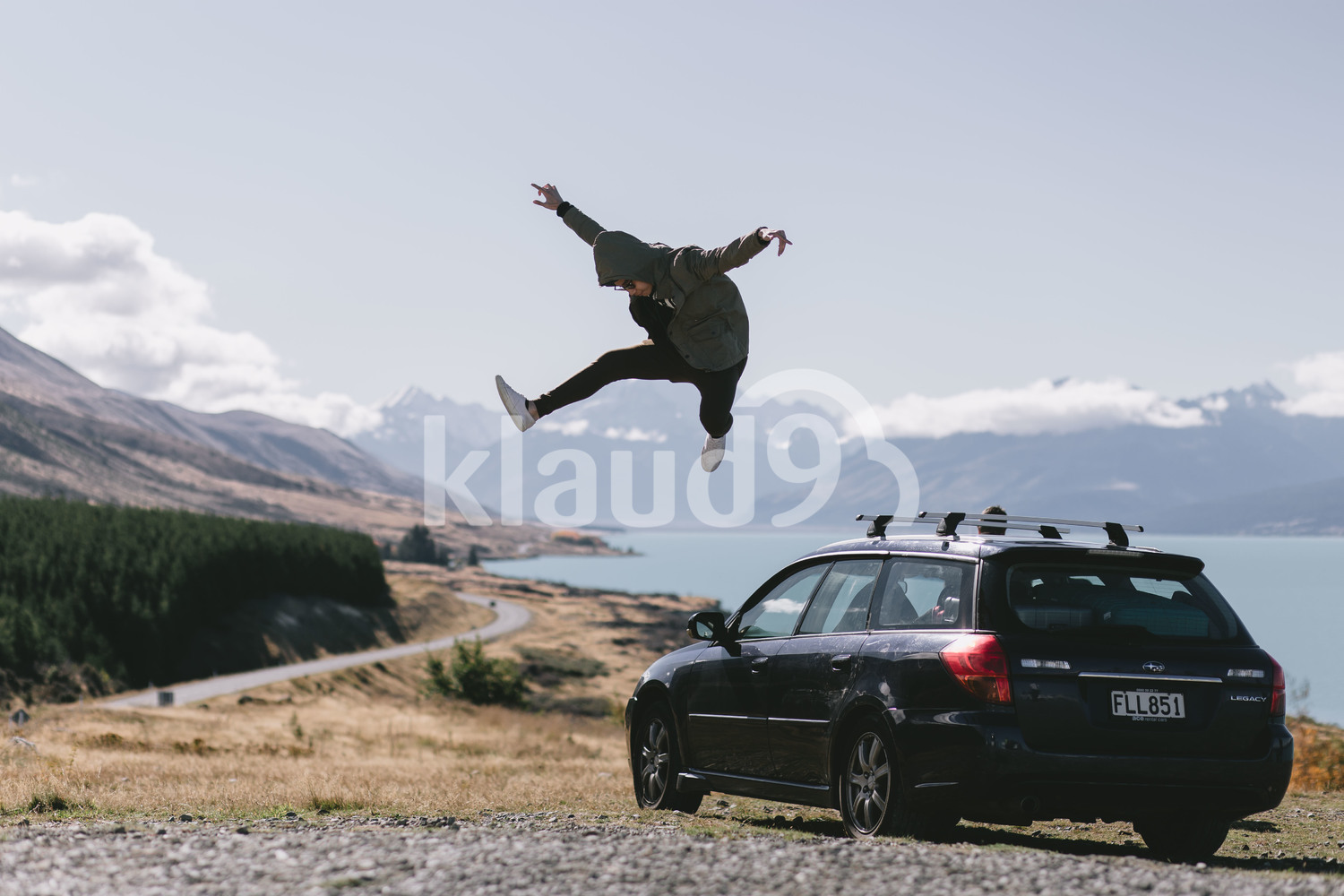 Young man jumping off a car in Milford Sound, New Zealand