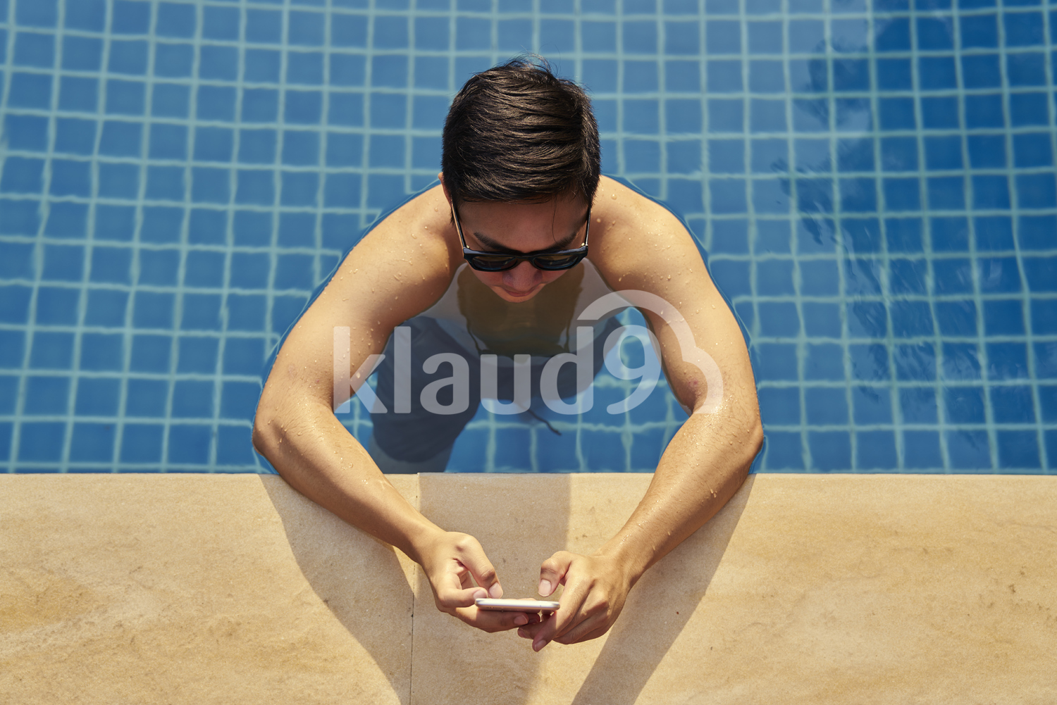 Young man taking photos with his mobile phone in the pool