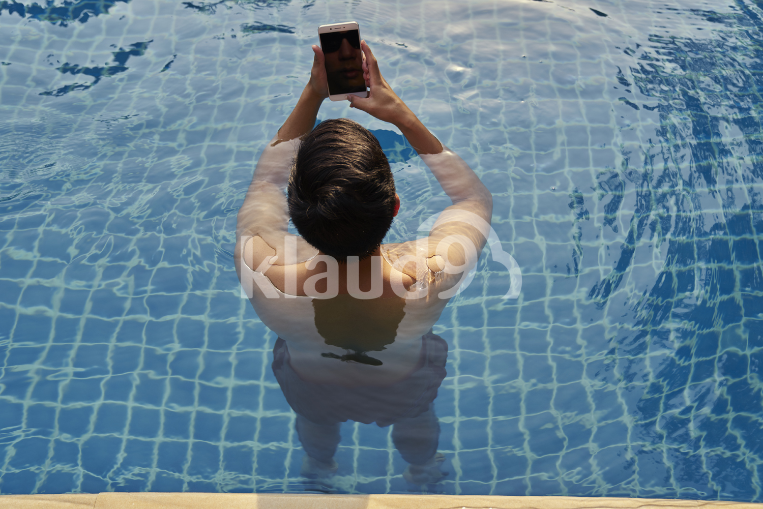 Young man taking photos with his mobile phone in the pool