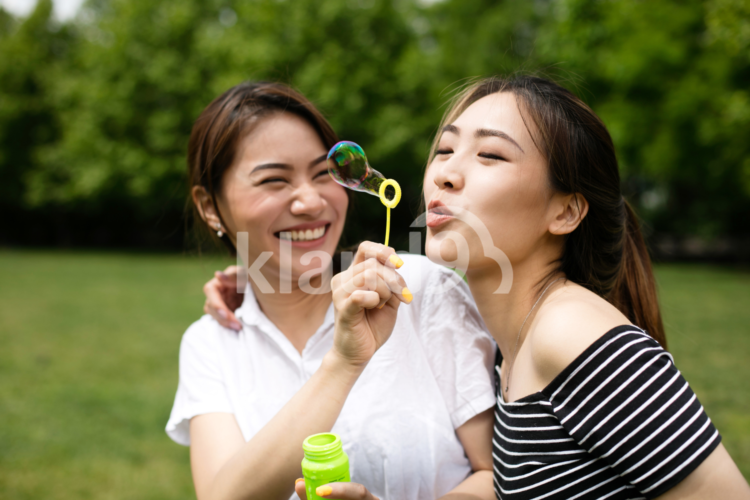 Cute asian girlfriends making soap bubbles in the park.