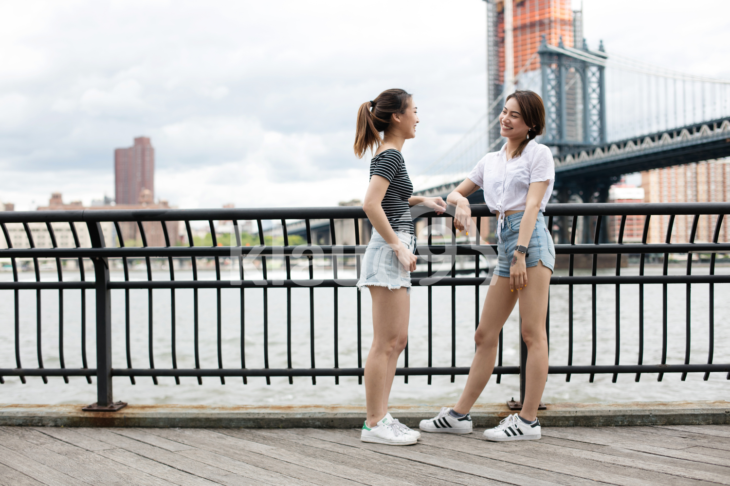 Asian girlfriends hanging out with the Brooklyn Bridge in the background when is summer.