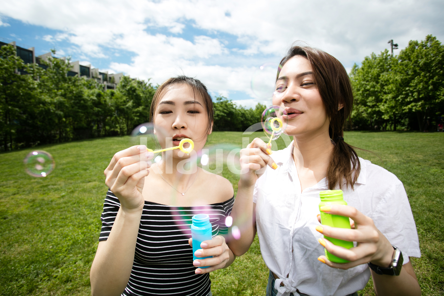 Cute asian girlfriends making soap bubbles in the park.