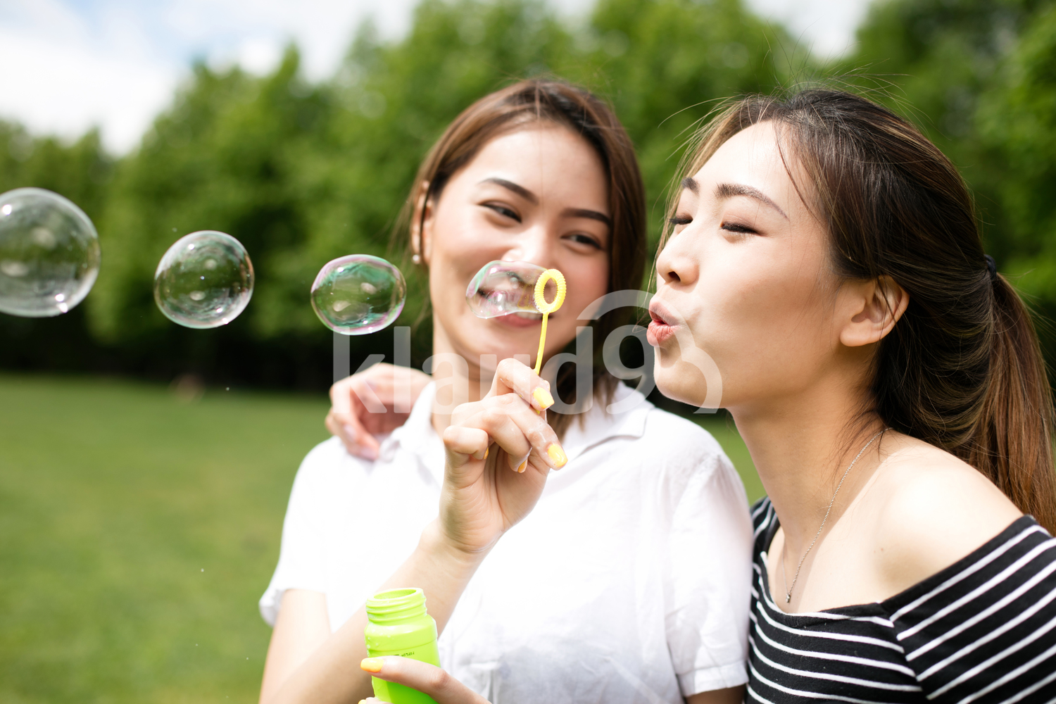Cute asian girlfriends making soap bubbles in the park.