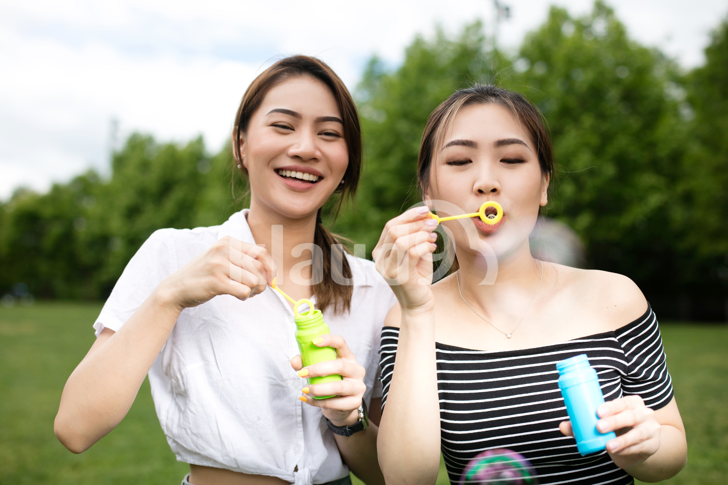 Cute asian girlfriends making soap bubbles in the park.