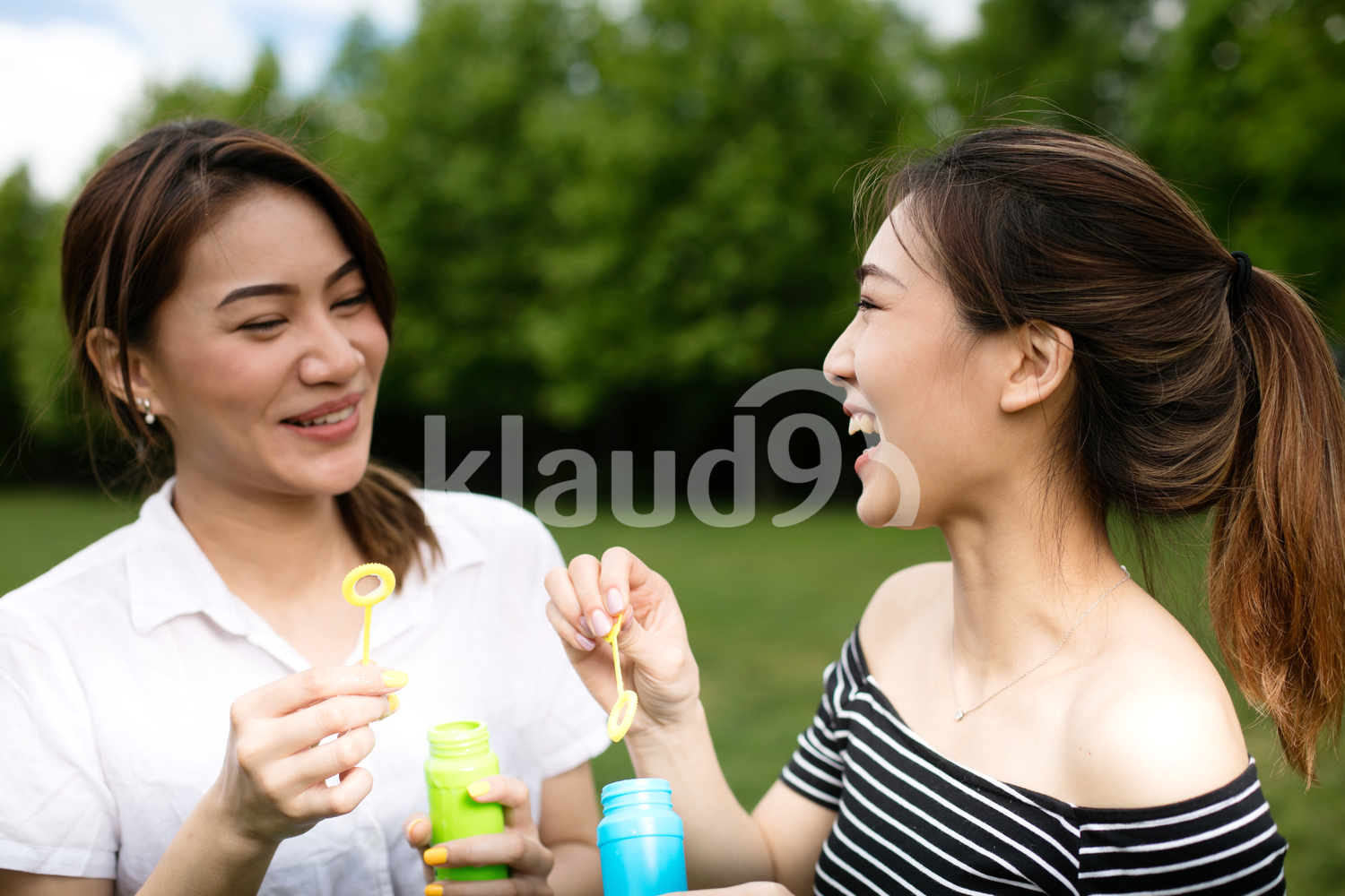 Cute asian girlfriends making soap bubbles in the park.