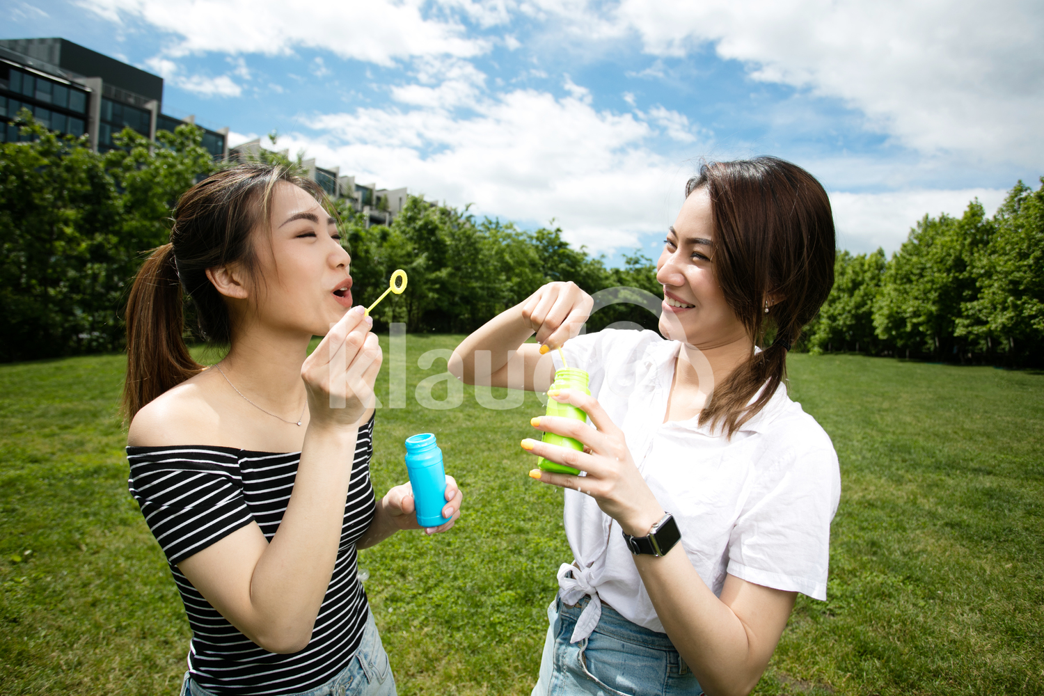 Cute asian girlfriends making soap bubbles in the park.