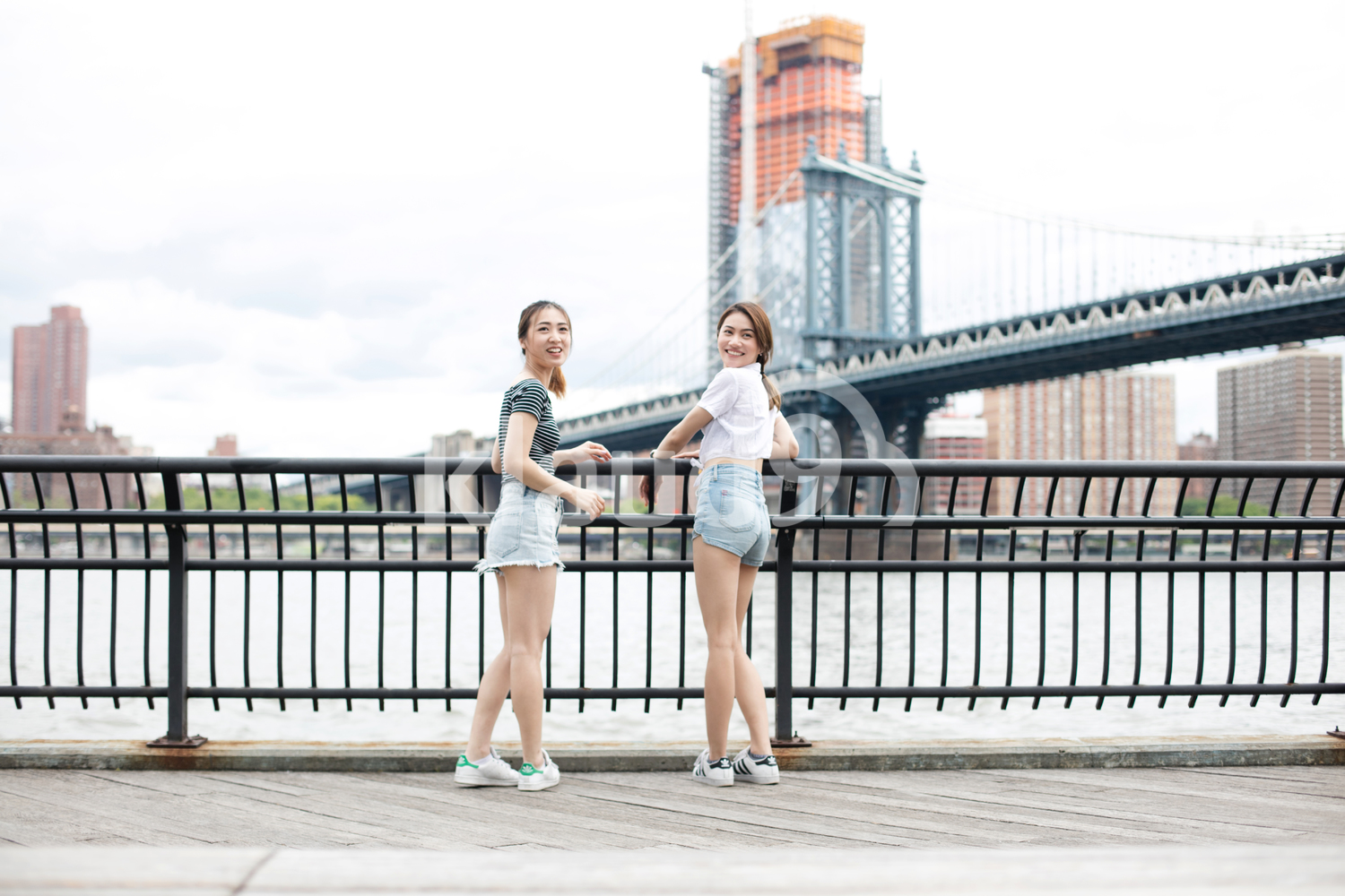 Asian girlfriends hanging out with the Brooklyn Bridge in the background when is summer.
