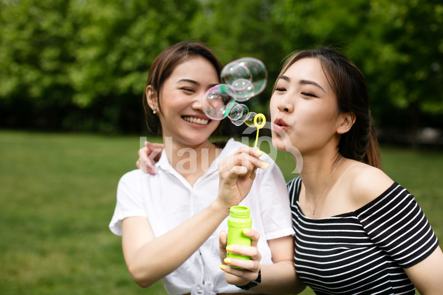Cute asian girlfriends making soap bubbles in the park.