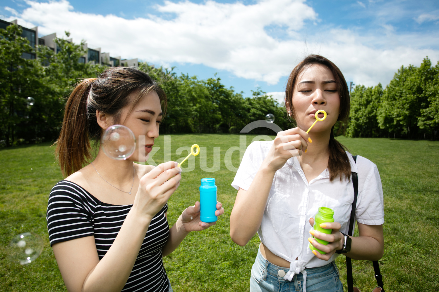 Cute asian girlfriends making soap bubbles in the park.
