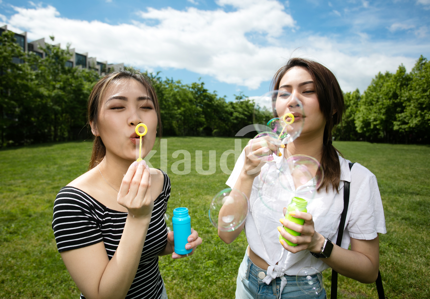 Cute asian girlfriends making soap bubbles in the park.