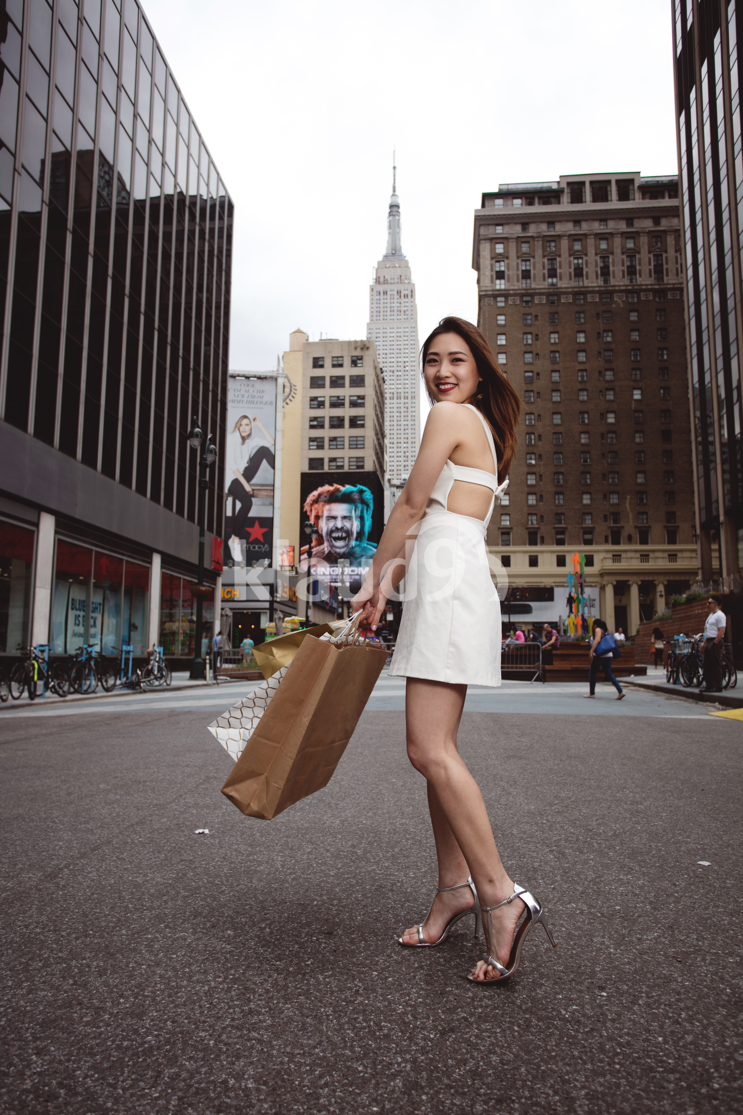 A beautiful elegant woman walking passing street and holding shopping bags with Empire state building.