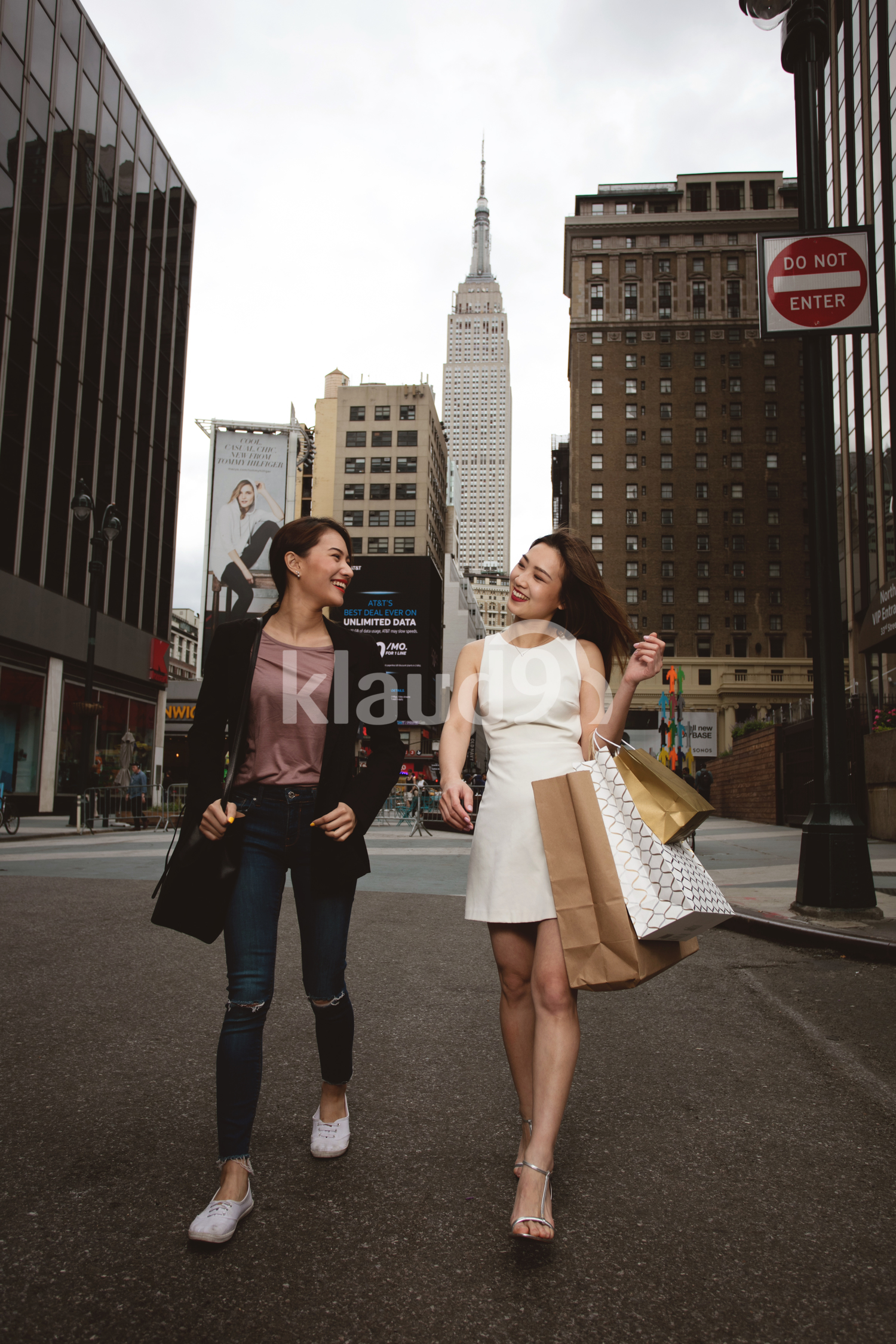 Two beautiful elegant women passing street and holding shopping bags with empire state behind.