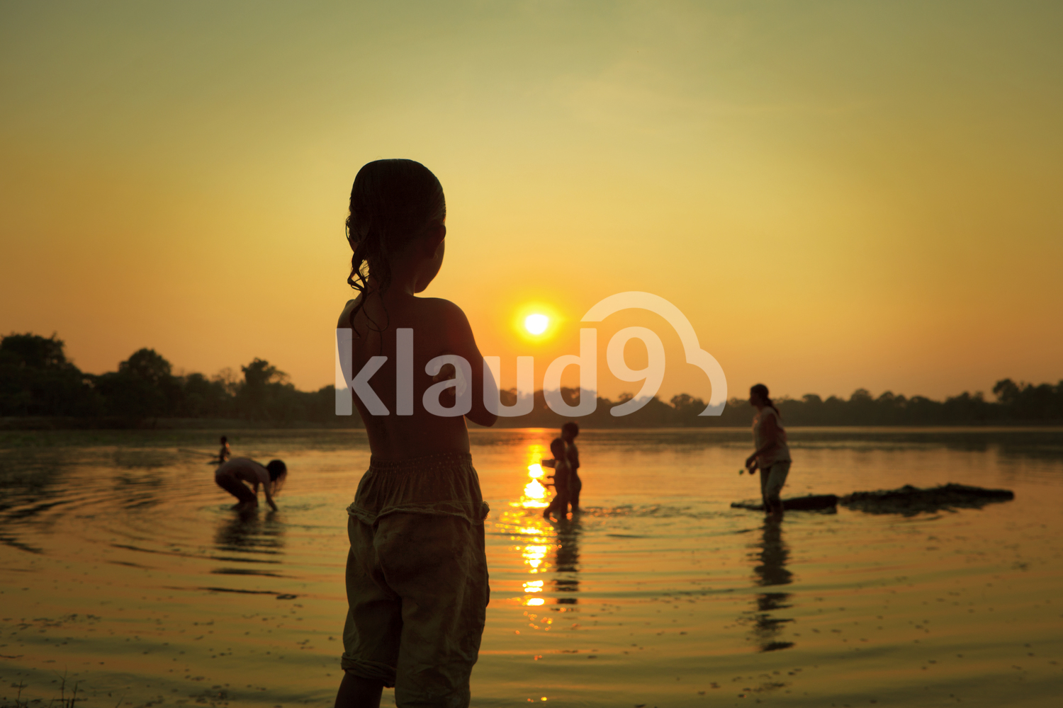Kids are playing, bathing and fishing in the Sra Srang Lake at Angkor Wat, siem Reap in Cambodia, while the sun sets over the lake.