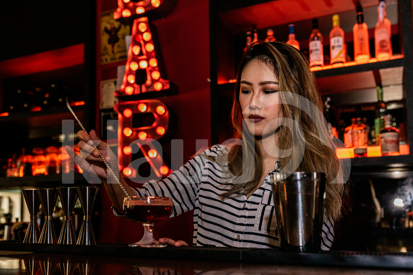 Asian bartender stirring drink using bar spoon
