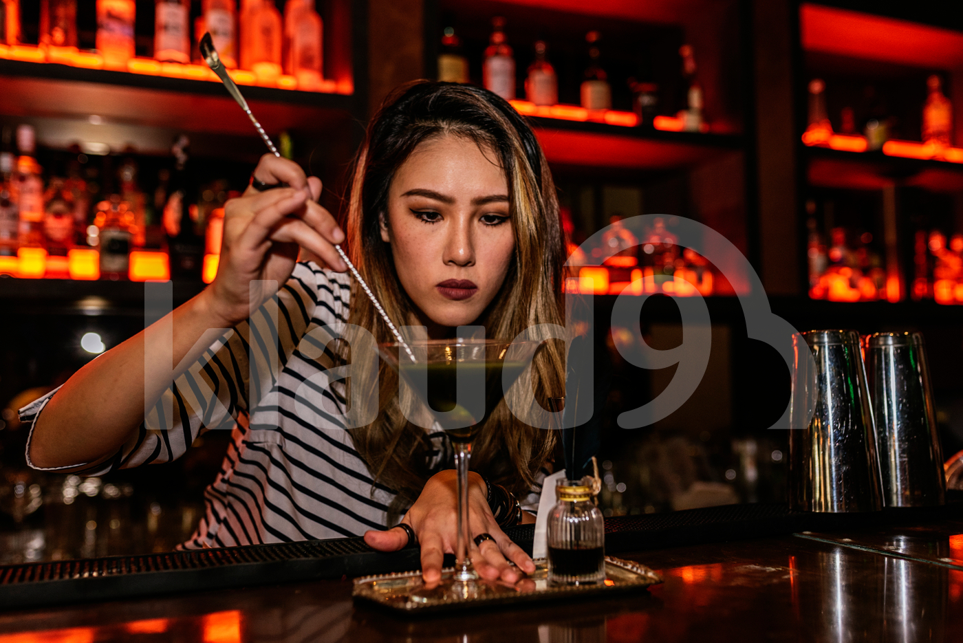 Asian bartender stirring cocktail drink using bar spoon