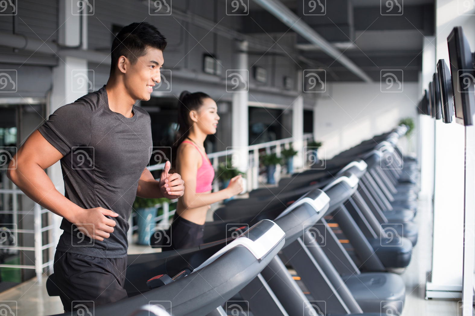 Young Chinese couple running on treadmills in gym 
