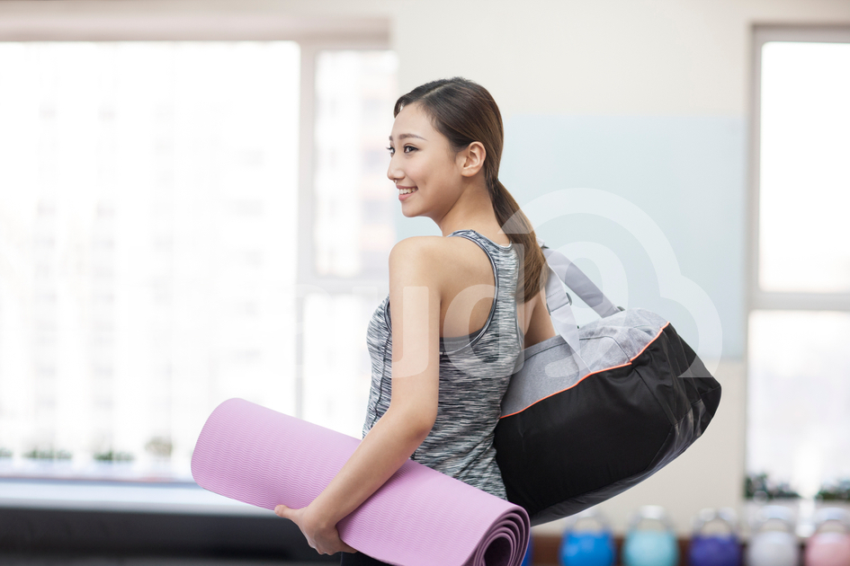 Young Chinese woman with yoga mat at gym