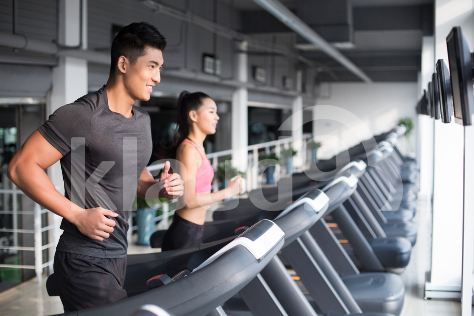 Young Chinese couple running on treadmills in gym