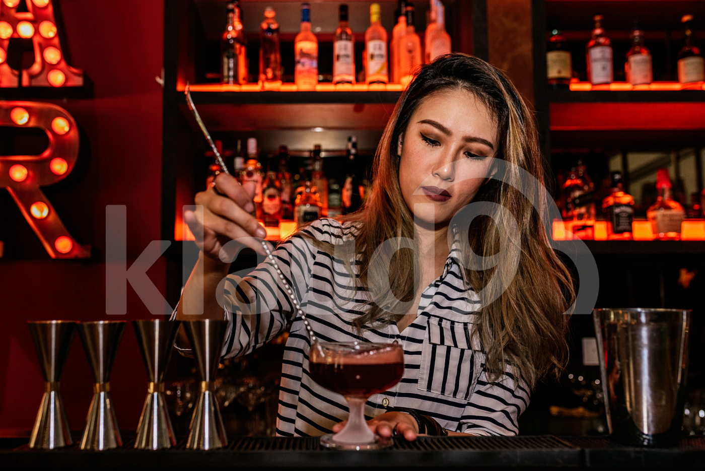 Asian bartender stirring drink using bar spoon
